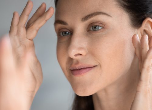 Woman looking at her face in the mirror after Bellafill treatments