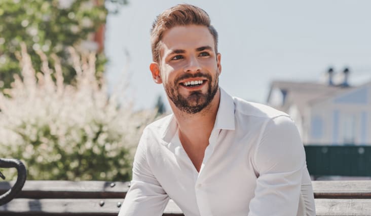 Smiling man wearing a white shirt, sitting on a park bench