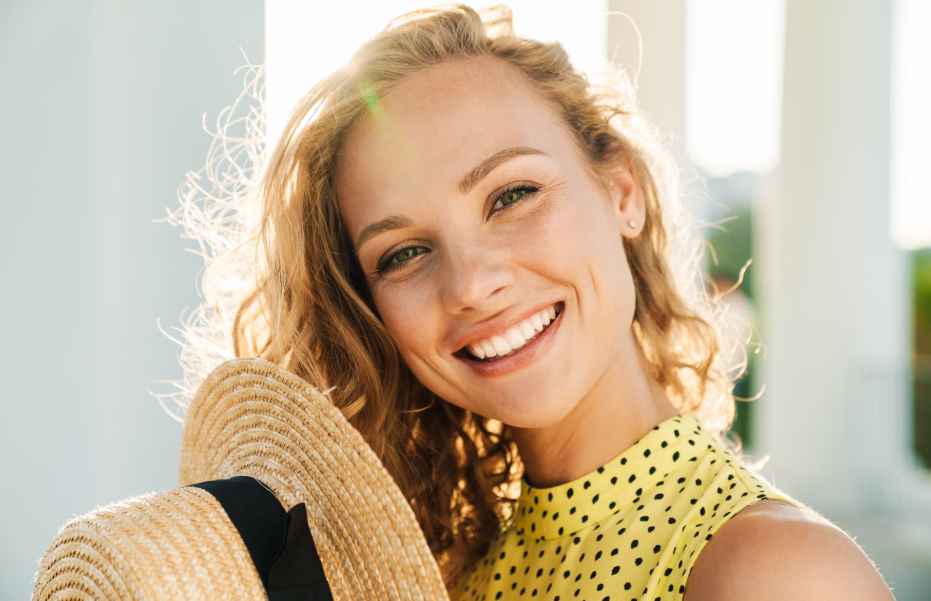 Woman in a yellow dress smiling and holding a sun hat